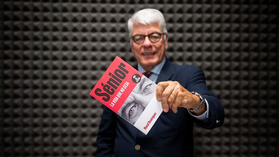 Manel Domínguez muestra su libro "Sénior. La vida que no cesa" (2ª edición). Portada roja y blanca con foto en blanco y negro.