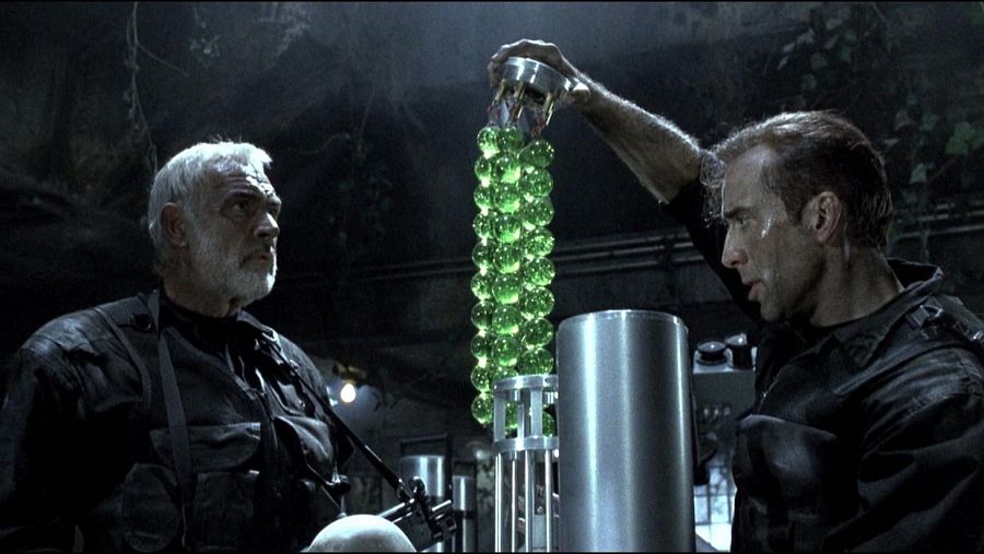 Sean Connery y Nicolas Cage en una escena de "La Roca". Cage sostiene un dispositivo con esferas verdes, en un entorno oscuro.