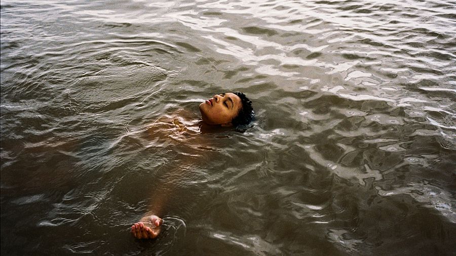 Fotografía de Nykiya Adams flotando en agua oscura y tranquila, parte de la obra "Bird".  Transmite serenidad y vulnerabilidad.
