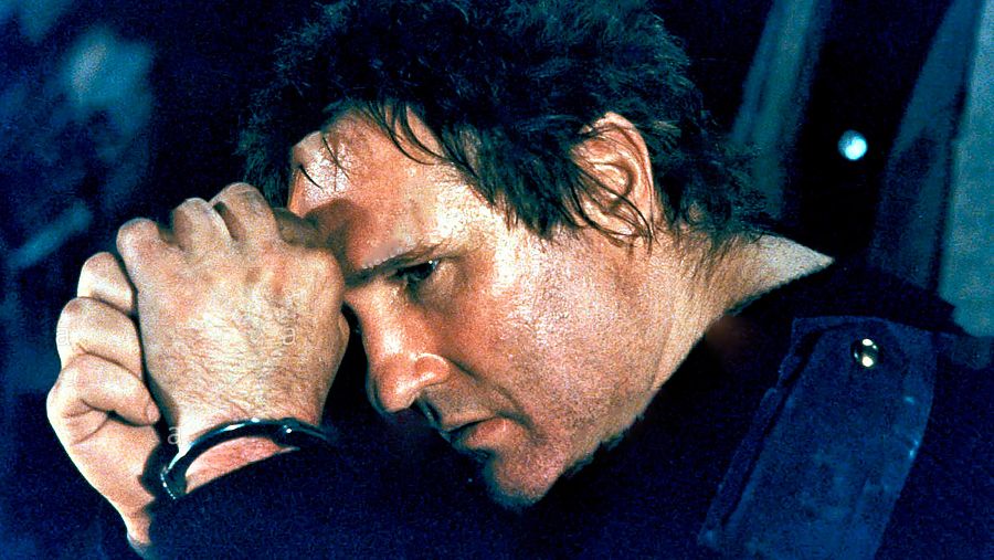 Imagen de Gerard Depardieu en una escena, posiblemente de "Pura formalidad", con las manos juntas a la altura de la frente y expresión seria. Prenda oscura, fondo borroso.