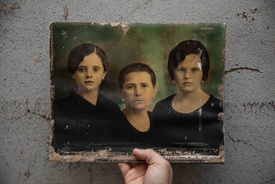 Fotografía antigua descolorida con tres personas vestidas de oscuro; dos mujeres y una persona más joven en el centro.  Fondo gris agrietado.