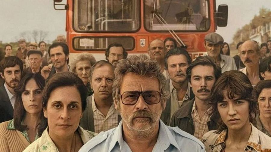 Grupo de personas con expresiones serias ante un autobús rojo antiguo en un entorno rural.  Imagen promocional de RTVE para "el47",  posiblemente una serie o película de temática histórica.