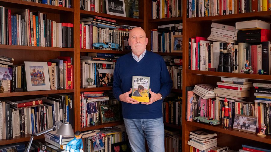 Màrius Carol presenta su libro "El nen dels escacs" en una imagen tomada en un entorno de biblioteca, rodeado de libros y objetos decorativos.
