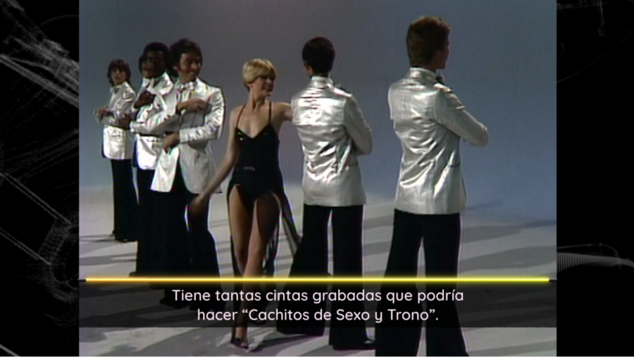 Bárbara Rey, con traje negro brillante, en un programa de TV, acompañada de cuatro bailarines con chaquetas plateadas.  Texto inferior alude irónicamente a grabaciones.