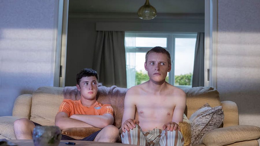 Escena de dos jóvenes en un sofá viendo la televisión.  Ambiente relajado, luz natural.  Imagen promocional de la serie "011 Horizontal" en RTVE Play.