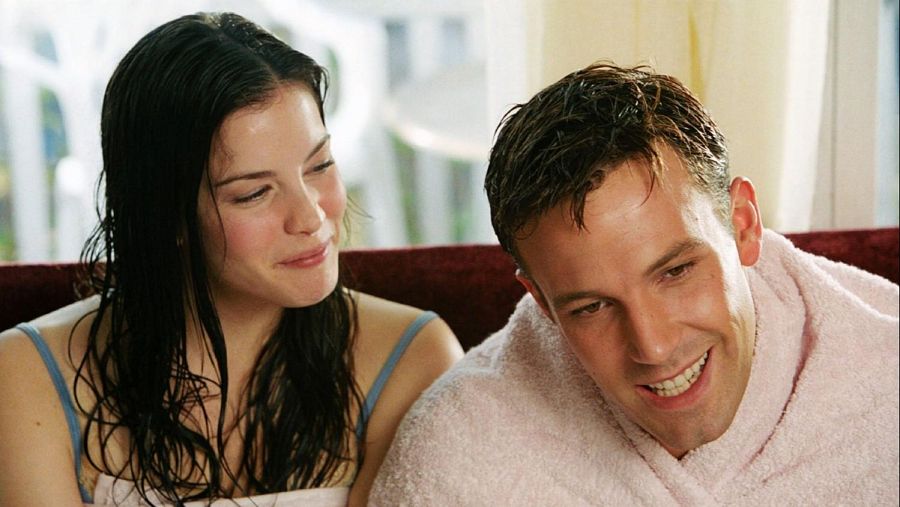 Escena íntima de Liv Tyler y Ben Affleck, recién duchados y envueltos en toallas, con sonrisas discretas.  Ambientación relajada.