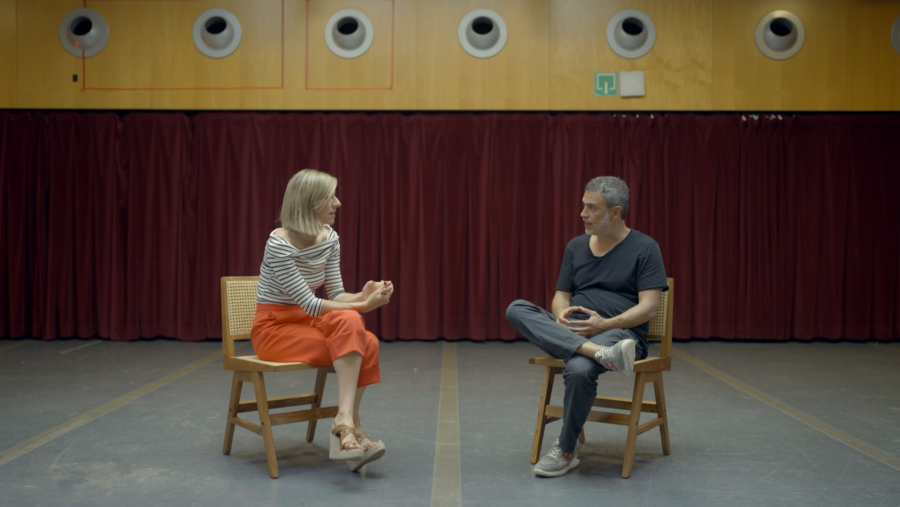 Entrevista a Julio Manrique en un escenario; él, con camiseta negra y pantalones grises, afirma que confía en su intuición para decidir. La entrevistadora viste una camiseta a rayas.