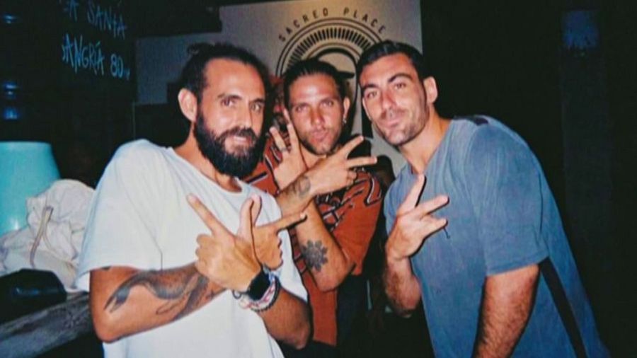 Tres hombres jóvenes, uno con barba y moño, posan haciendo el gesto de la paz.  La imagen, con poca luz, incluye el texto "Justicia para Diego".