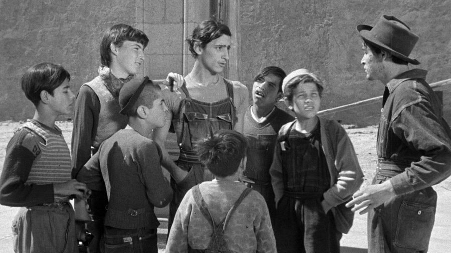Escena en blanco y negro de "Los olvidados": ocho niños y jóvenes en entorno urbano, con vestimenta sencilla, interactuando entre sí.  Ambiente de pobreza y marginalidad.