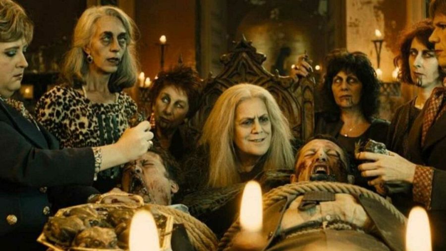 Mujeres disfrazadas de brujas realizan un ritual alrededor de un hombre atado en una escena oscura e iluminada con velas.  Sangre simulada en la escena.
