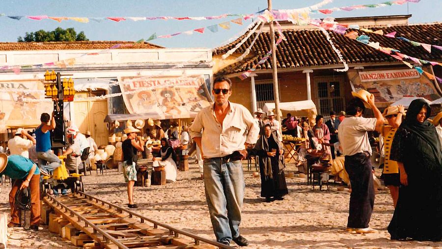 Félix Murcia, director de arte, en el rodaje de una película ambientada en una plaza festiva con vías de tren, extras con vestuario de época y carteles que anuncian "Fiesta Cubana" y "Danzón-Santiago".