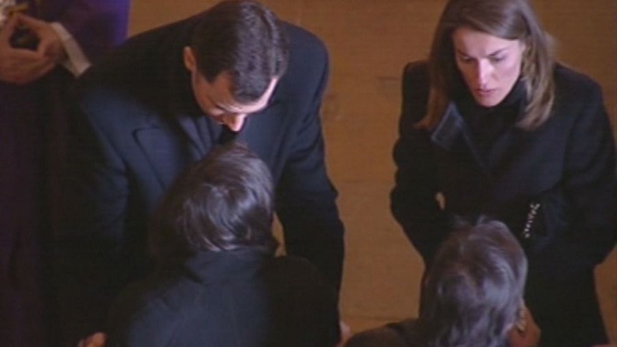 Los Príncipes de Asturias, Felipe y Letizia, vestidos de luto, asisten a un funeral.  Él da el pésame; ella observa con semblante serio.  Dos personas más están presentes.