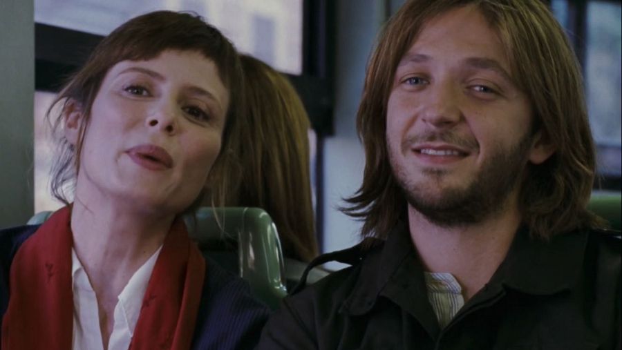 Aitana Sánchez Gijón y Silvio Muccino en una escena de autobús de la película "Háblame de amor". Ella viste camisa blanca y bufanda roja; él, chaqueta oscura. Conversación.