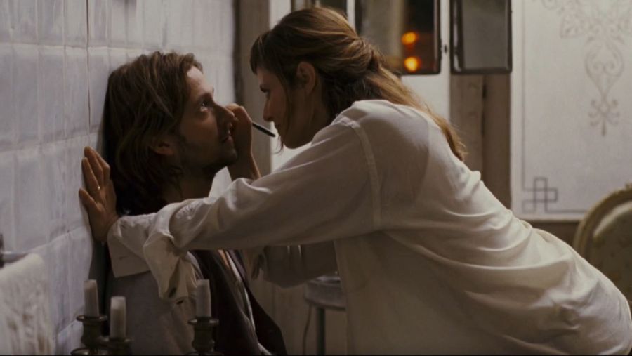 Aitana Sánchez Gijón maquilla a Silvio Muccino en una escena íntima de "Háblame de amor", en un espacio con azulejos y luz tenue.