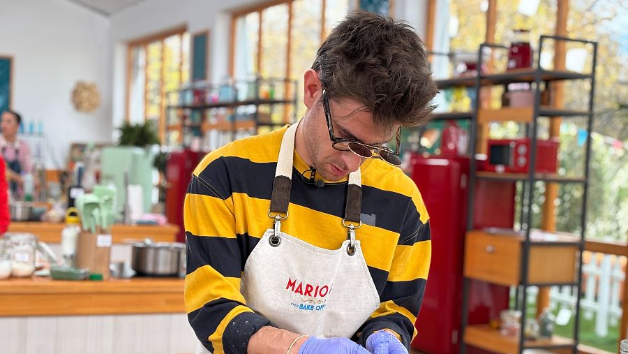 Mario Marzo en el séptimo programa de 'Bake Off', con camiseta a rayas, delantal blanco con su nombre bordado y guantes azules, preparando una receta.