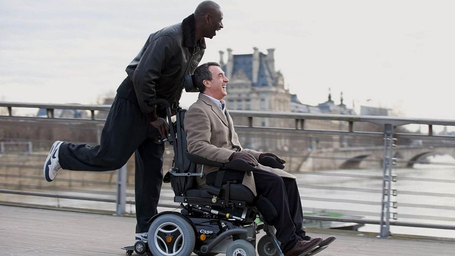 François Cluzet y Omar Sy, en una escena alegre de "Intocable", comparten un momento de complicidad; uno en silla de ruedas motorizada, el otro empujándola con energía.