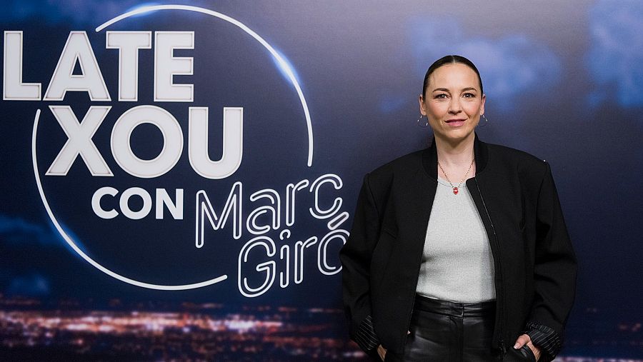 Fotografía promocional de Leonor Watling para el programa "Late Xou".  La actriz viste chaqueta negra, camiseta gris y pantalones negros, mirando a cámara con expresión seria.