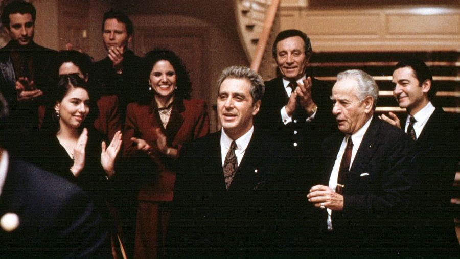 Escena de 'El Padrino de Mario Puzo, Epílogo: La muerte de Michael Corleone' donde Al Pacino, como Michael Corleone, es aplaudido por un grupo en un ambiente elegante. Se observa una bola de billar.