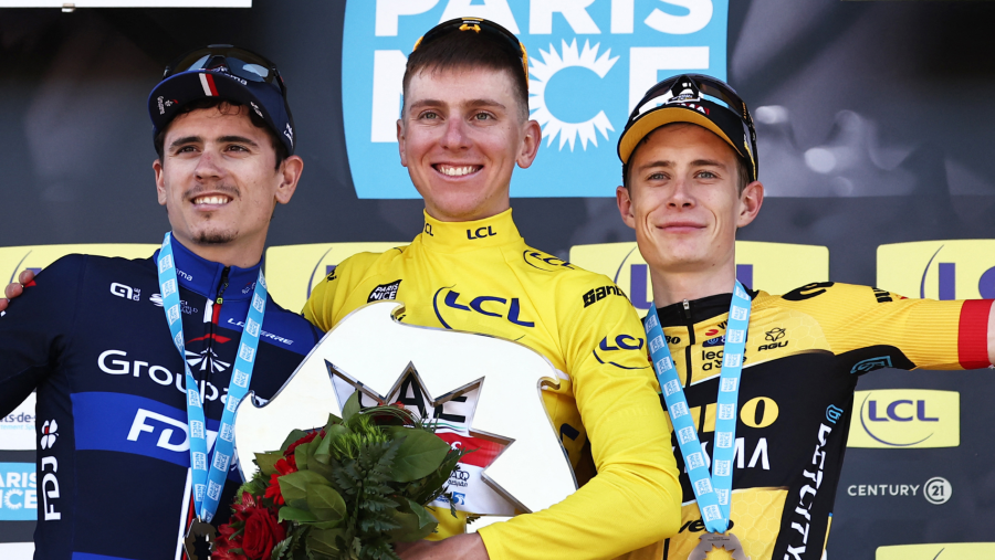 Podio de ciclismo: tres ciclistas con medallas sonríen; el del centro, con maillot amarillo, sostiene un trofeo.