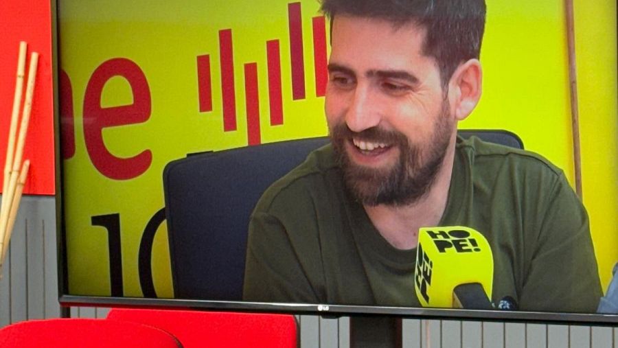 Entrevista a Javier Peña en el podcast "HOPE! Estamos a tiempo".  Se le ve sonriente, con camiseta verde oliva, frente a un micrófono con etiqueta amarilla del podcast. Fondo amarillo con barras rojas.