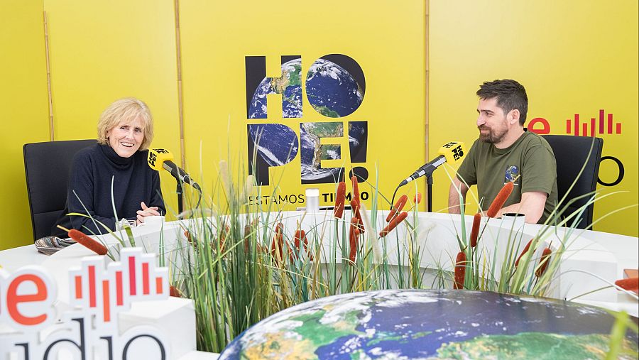 Entrevista en estudio de radio a Mercedes Milá y Javier Peña con fondo amarillo, logo Cadena SER y el mensaje "HOPE!" con imagen de la Tierra.  Mesa con plantas y maqueta del planeta.