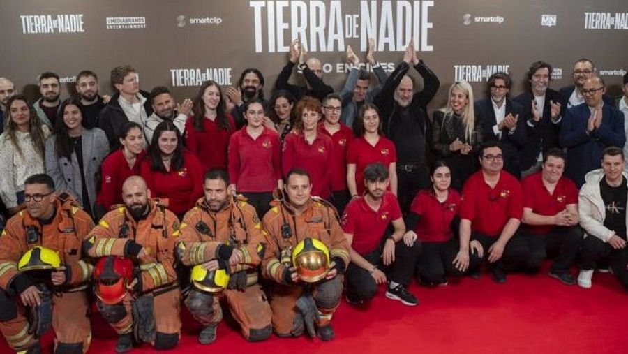 Alfombra roja en la premiere de 'Tierra de nadie'. Bomberos con sus uniformes y personas con camisetas rojas con el logo de la película posan para una foto.