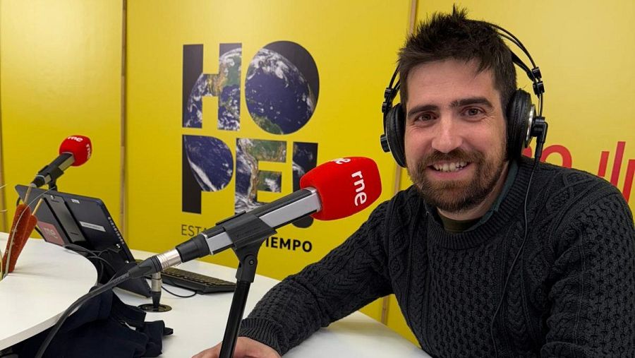 Javier Peña, en un estudio de radio, sonríe a cámara durante una grabación o entrevista. Lleva jersey oscuro y auriculares; a su alrededor, equipo de grabación y logotipos de su programa y RNE.