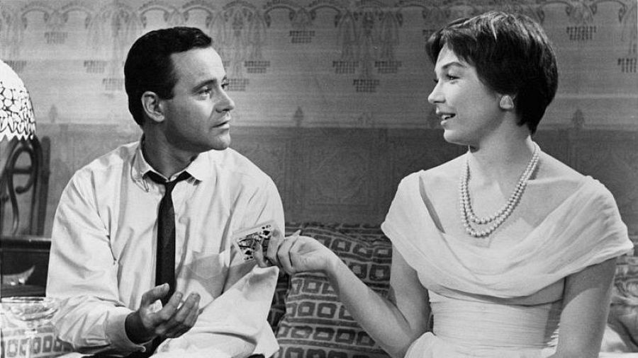 Jack Lemmon y Shirley MacLaine en una escena de "El Apartamento". Él gesticula; ella sostiene una carta.  Ambiente de apartamento.