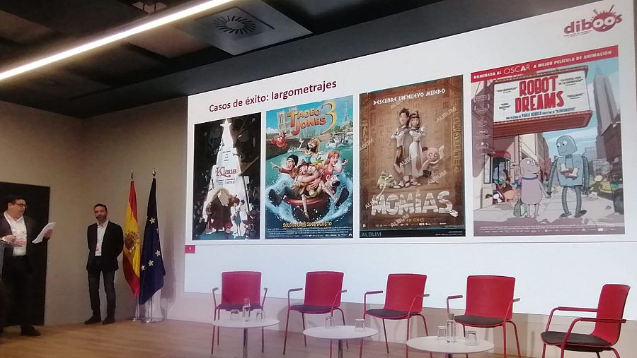 Presentación del Libro Blanco de la Animación 2024 en Madrid. Dos hombres en escenario, pantalla con pósters de películas animadas y mesa redonda preparada.