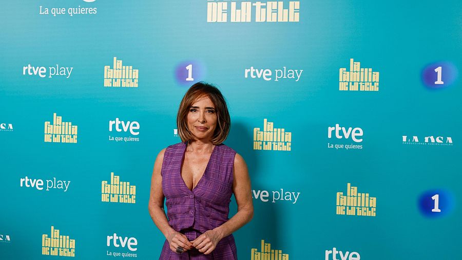 Presentadora con traje morado en photocall turquesa con logotipos de RTVE y 'La Familia de la Tele'.