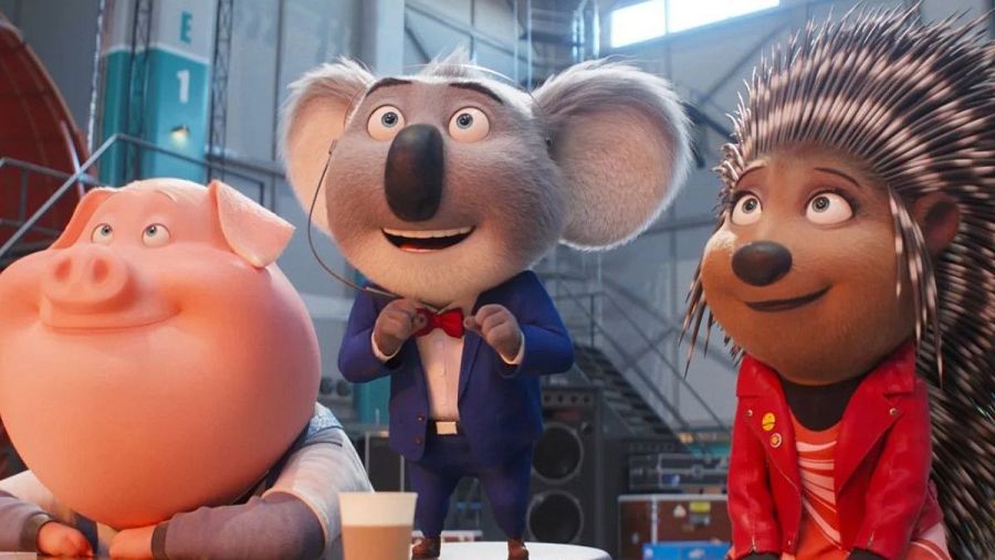 Tres personajes de "Canta" (cerda rosa, koala en traje azul y puercoespín con chaqueta roja) en el backstage, listos para actuar. Se ve equipo de sonido y escalera.