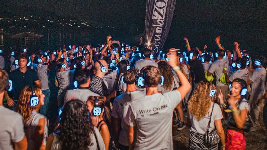 Fiesta silenciosa nocturna: multitud bailando con auriculares inalámbricos. Algunos asistentes llevan camisetas con la frase "Write On Me".