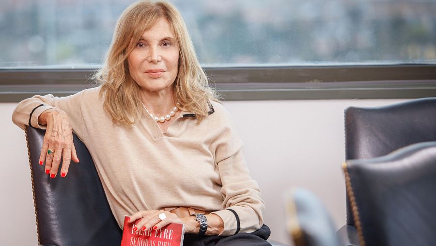 Pilar Eyre en entrevista, con libro "Señoras del buen morir", jersey beige, collar de perlas y anillo verde.  Fotografía tomada durante programa de radio.