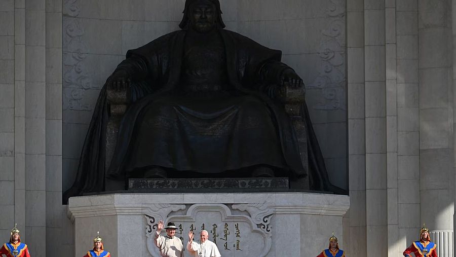 El Papa Francisco y un acompañante saludan una gran estatua de Gengis Kan, custodiada por guardias en vestimenta tradicional mongola.