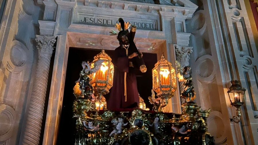 El Cristo del Gran Poder sale en procesión, su paso dorado iluminado por candelabros,  de una iglesia con la inscripción "JESUS DEL PODER".