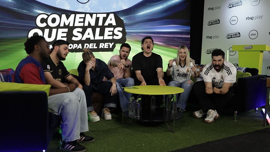 Grupo de jóvenes reaccionando a un evento deportivo en un estudio de televisión con decoración de campo de fútbol. Se aprecian expresiones de alegría, tensión y sorpresa.
