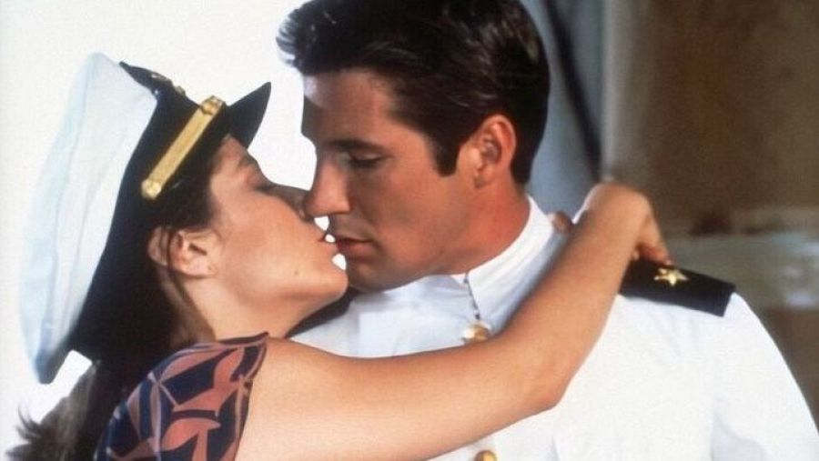 Richard Gere y Debra Winger se besan apasionadamente en una escena romántica. Él viste uniforme blanco; ella, blusa estampada y gorra de marinero.