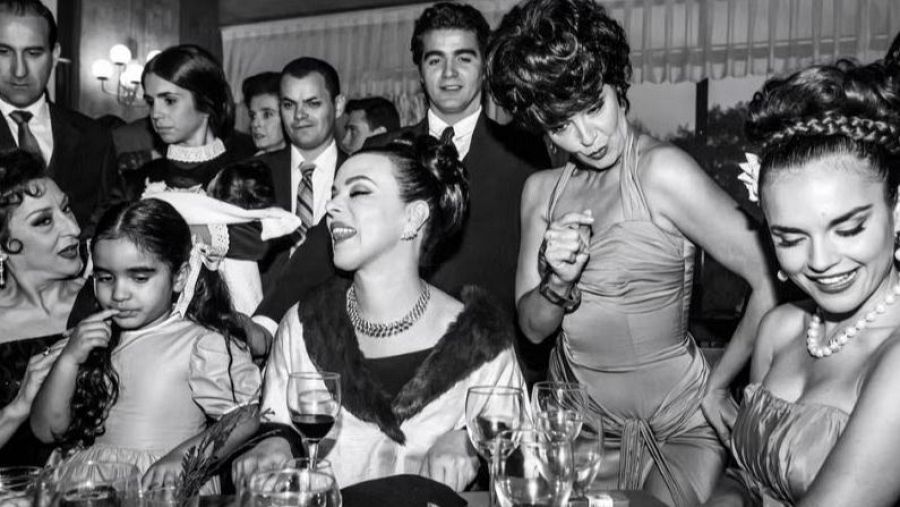 Imagen en blanco y negro de una fiesta de los años 60. Melody, caracterizada como Carmen Sevilla, sonríe; otra mujer, con similar caracterización, está en el centro.