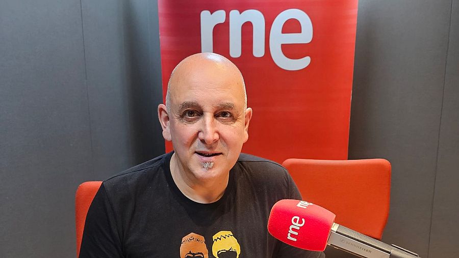 Periodista en estudio de radio RNE, con camiseta negra y micrófono con logo de la emisora. Banner rojo con logo visible al fondo.