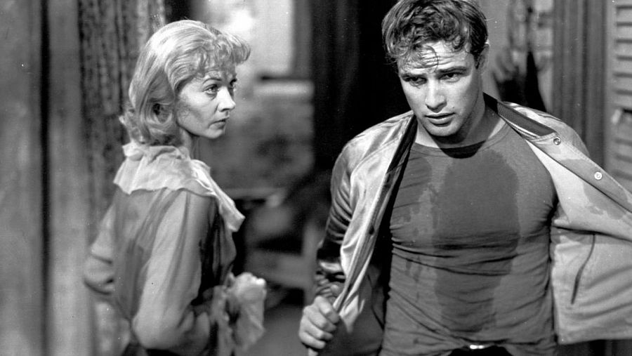 Marlon Brando y Vivien Leigh en una escena dramática; él, con chaqueta y camiseta húmeda, ella, con blusa clara, mirándolo con expresión preocupada.