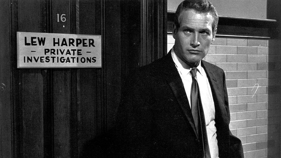 Paul Newman, en su papel de Lew Harper, investigador privado, aparece serio en la entrada de una oficina con un cartel que indica su profesión.