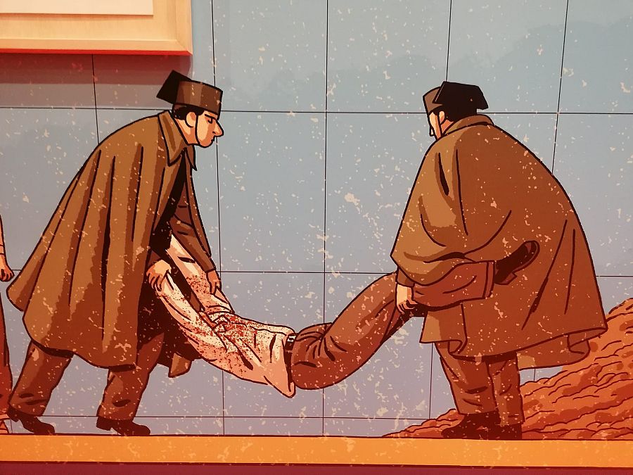 Detalle de mural: tres figuras, dos cargando a una tercera con ropa marrón y manchas que parecen sangre, sobre fondo de azulejos claros. Escena dramática.