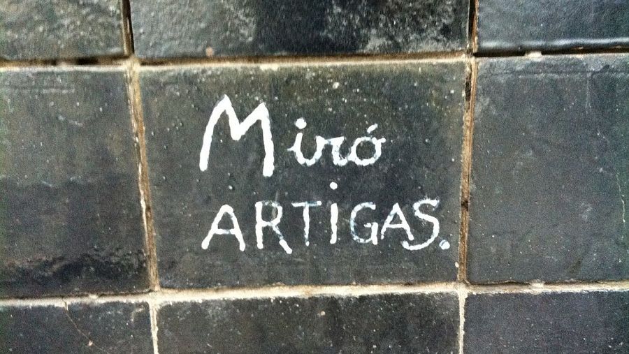 Firmas pintadas en blanco sobre azulejos oscuros: "Miró" sobre "Artigas". Posible documentación de la colaboración artística entre ambos.