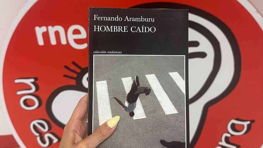 Portada del libro "Hombre caído" de Fernando Aramburu, colección "Andanzas", con imagen de un hombre cayendo.  Una mano lo sostiene, con una uña amarilla. Fondo con logo RNE.