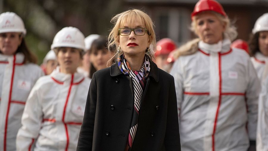 Cate Blanchett, con abrigo negro y gafas, entre mujeres con trajes de protección blancos y rojos.  Escena de película con ambiente de trabajo peligroso.