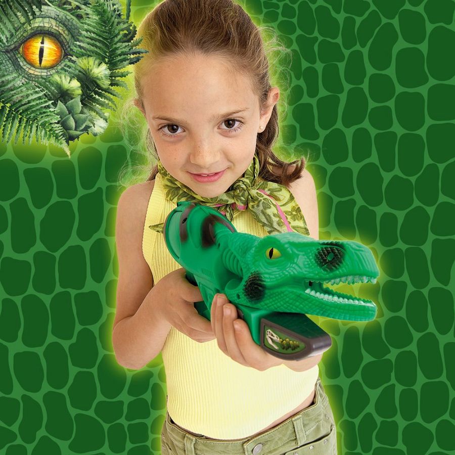 Niña con camiseta amarilla y pantalones verde oliva, sostiene una pistola de juguete verde con forma de dinosaurio y mira a la cámara sonriendo.