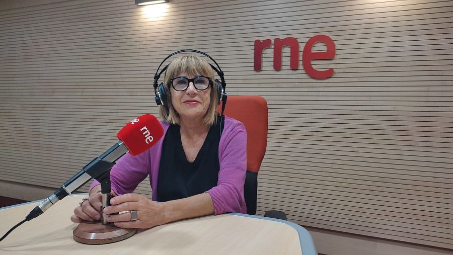 Periodista en estudio de radio con micrófono y auriculares, frente a un fondo con el logo de la emisora y listones horizontales.