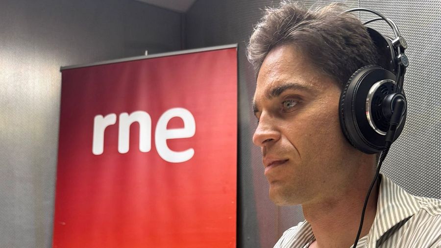 Persona con auriculares en estudio de radio, posiblemente RNE, con panel rojo y logo visible.  Emisión relacionada con noticias culturales.