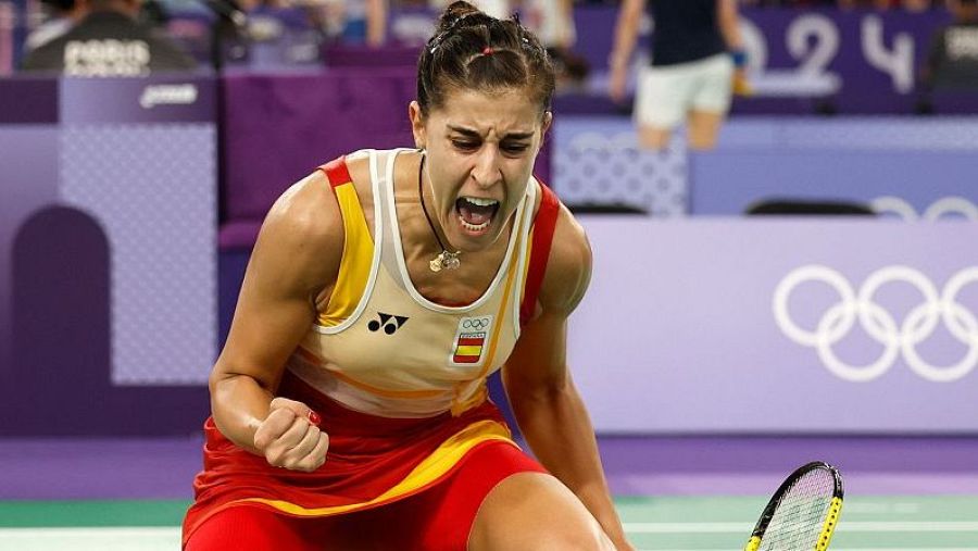 Celebración eufórica de una deportista con camiseta roja y amarilla, puño cerrado y boca abierta.  Fondo con anillos olímpicos.