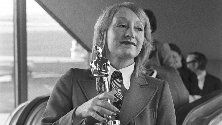 Yvonne Blake, ganadora del Óscar en 1971, posa con la estatuilla.  Viste traje chaqueta, camisa blanca y corbata oscura con un diseño similar a la bandera estadounidense.